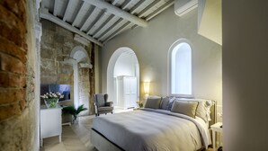 A bedroom with a large bed, a TV, a chair, and a desk. - The Gilded Residence (Lucca)
