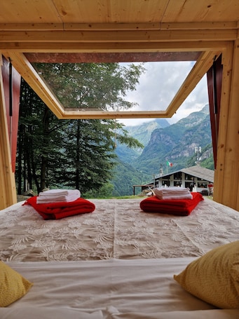 A room with a bed, a view of mountains, and a wooden ceiling.. Glamping Alpe Campo Rimasco