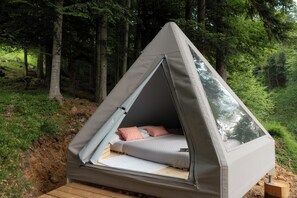 A tented accommodation with a bed, a window, and a view of the forest.
