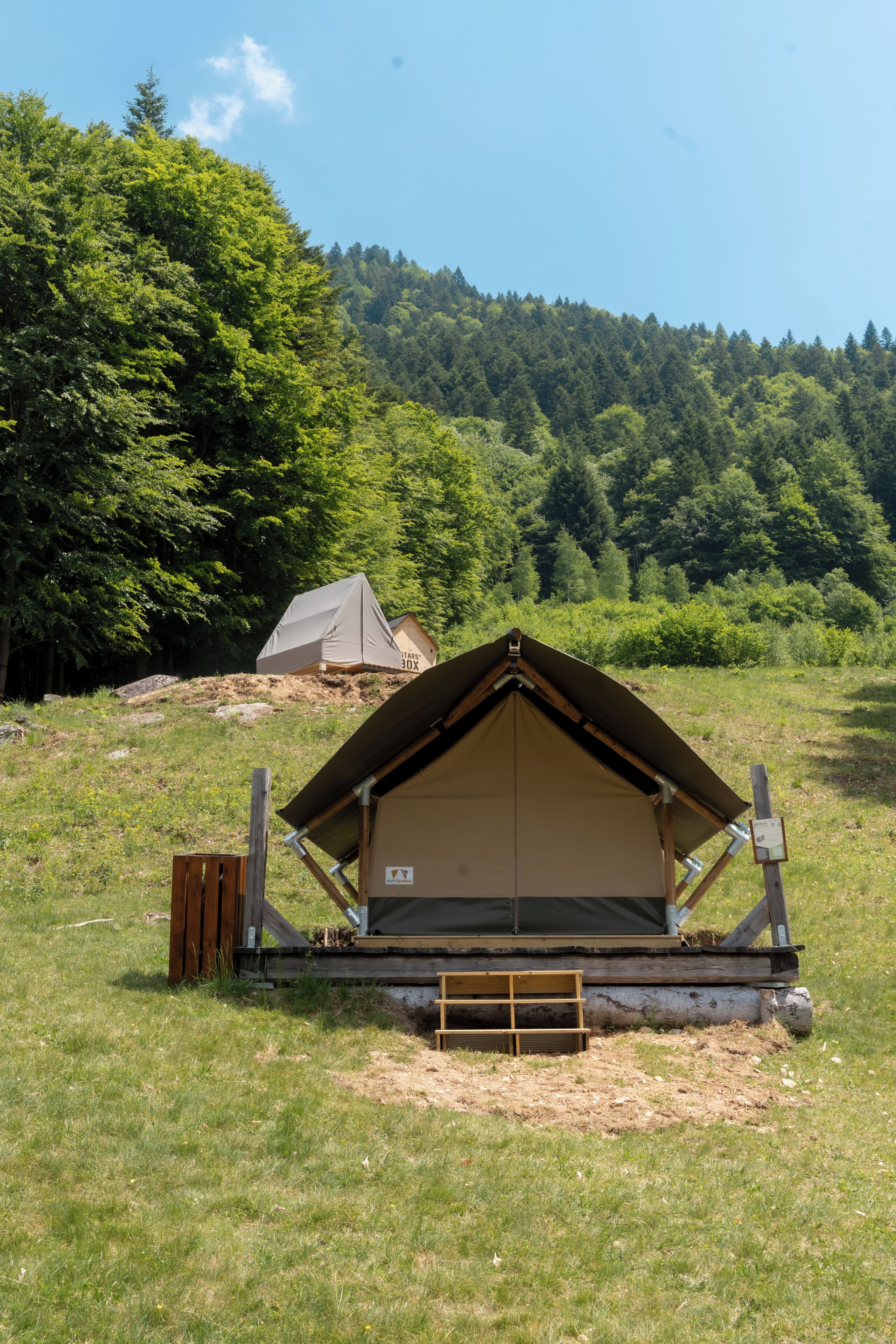 Ein Campingplatz mit Zelten in einem grünen Feld, im Hintergrund Bäume.