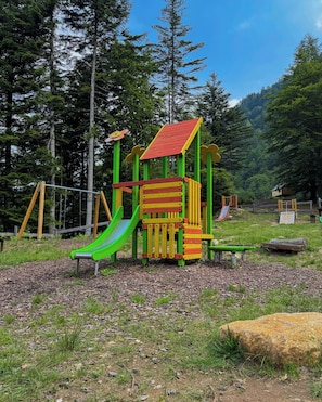 A playground with a slide, climbing structures, and a small building.