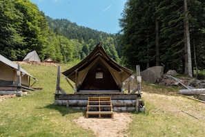 A small, single-room cabin with a sloped roof, a wooden bench in front, and a log base. - Glamping Alpe Campo Rimasco (Rimasco)