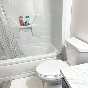A bathroom with a bathtub, toilet, and shower curtain. - A cozy haven at the heart of the city and a minute drive to the airport (St. John's)
