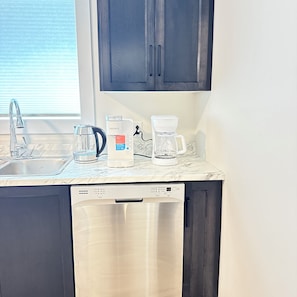 A kitchen with a dishwasher, a coffee maker, and a kettle on the countertop. - A cozy haven at the heart of the city and a minute drive to the airport (St. John's)
