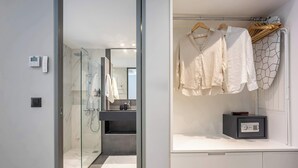 Un baño moderno con cabina de ducha de vidrio, un tocador blanco con dispensador de jabón negro y un perchero con prendas blancas.
