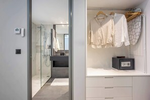 A modern bathroom with a glass shower enclosure, a white vanity with a black soap dispenser, and a hanging clothes rack with white garments. - Cozy Spacious Studio  Prime Psyri  AcropolisView (Athens)