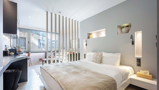 Una habitación de hotel moderna con cama, mesita de noche y un espacio de escritorio.