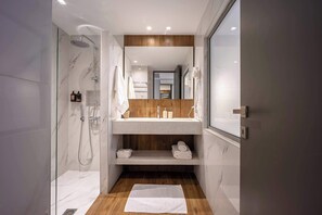 Ein modernes Badezimmer mit einer begehbaren Glasdusche, einem Waschtisch mit Spiegel und einem Holzregal.