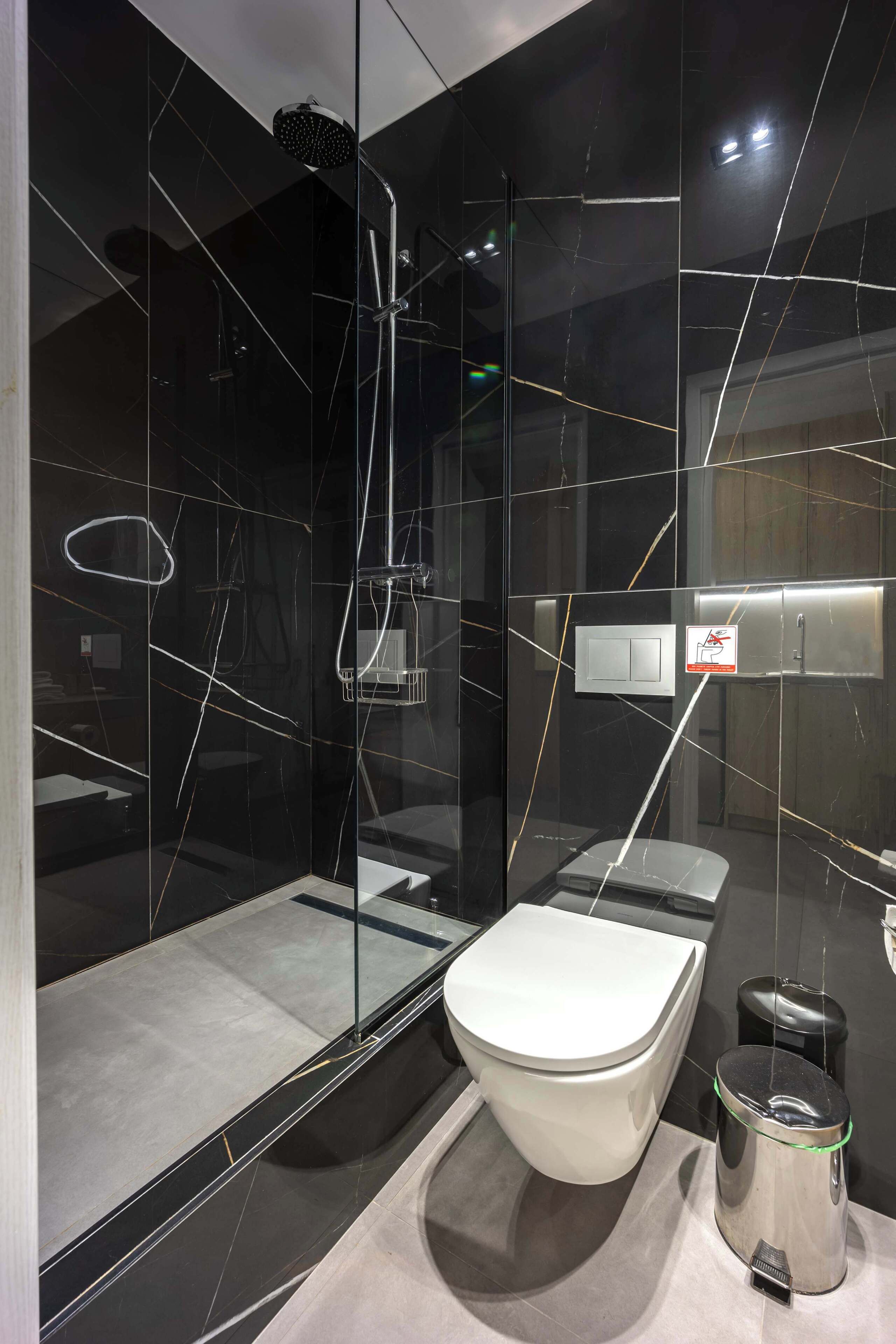 A modern bathroom with a glass-enclosed shower, a toilet, and a trash bin.