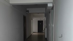 Un long couloir étroit aux murs blancs et au sol marron, qui mène à une porte au bout.