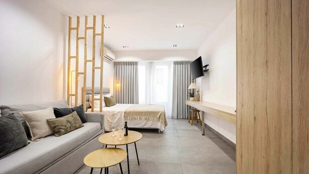 Une chambre d’hôtel moderne équipée d’un canapé, d’une petite table ronde, d’un lit, d’un téléviseur fixé au mur et d’une cloison en bois.