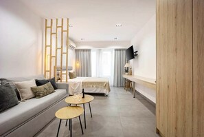 A modern hotel room with a sofa, a small round table, a bed, a TV mounted on the wall, and a wooden partition. - Generous Studio Syntagma | Worn Building Entrance (Athens)