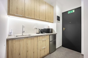 A modern kitchen with wooden cabinets, a stainless steel sink, a coffee maker, a kettle, a microwave, and a black refrigerator. - Generous Studio Syntagma | Worn Building Entrance (Athens)