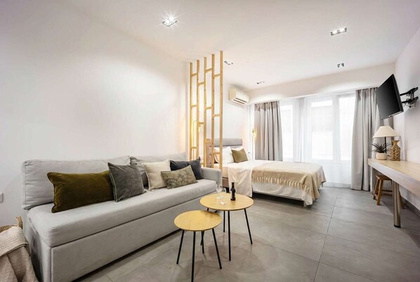 A modern hotel room with a sofa, a bed, a small round table, a TV mounted on the wall, and a window with curtains. - Generous Studio Syntagma | Worn Building Entrance (Athens)