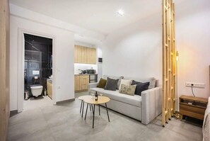 A modern living room with a sofa, a coffee table, and a kitchen in the background. - Generous Studio Syntagma | Worn Building Entrance (Athens)