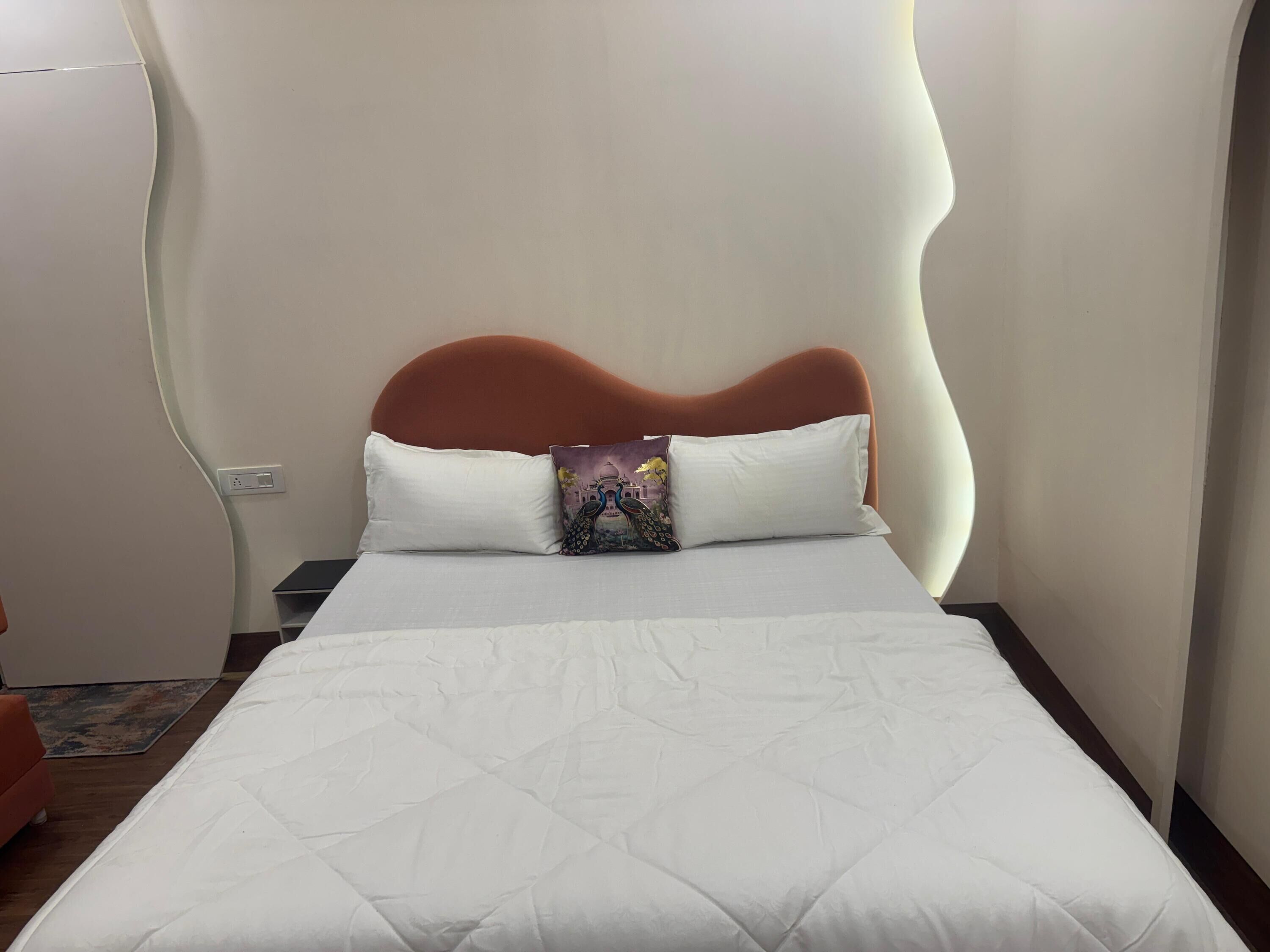 Una cama con colcha blanca, cabecera marrón y dos almohadas, una con diseño colorido.