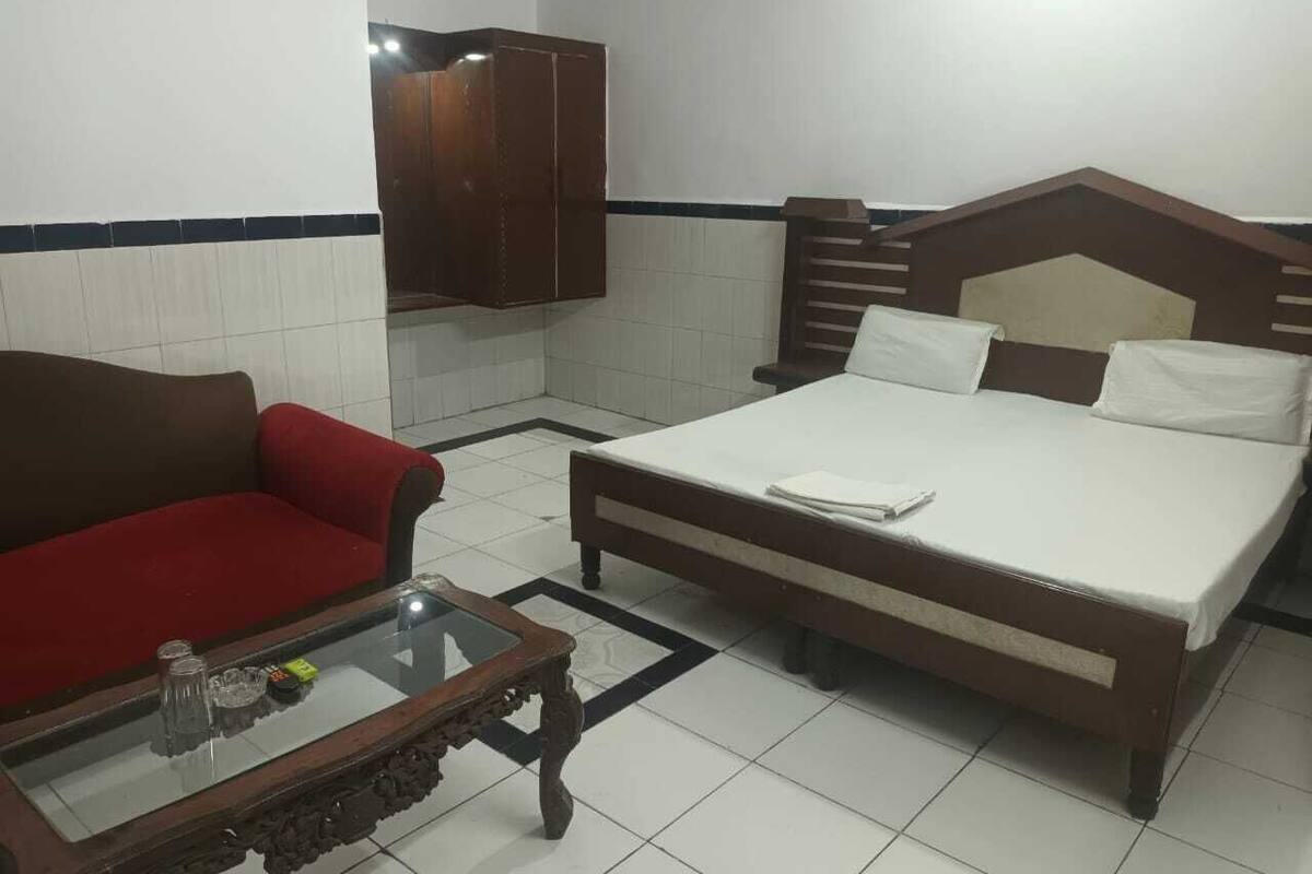 A room with a bed, a red sofa, a glass-top coffee table, and a wooden cabinet.