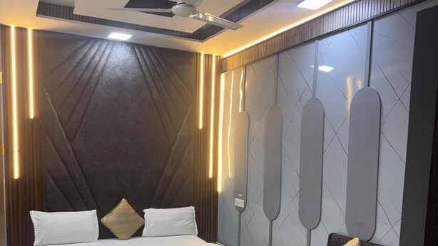 A modern bedroom with a large bed, a ceiling fan, and wall-mounted lighting. - Hotel American (Saharanpur)