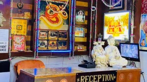 A reception desk with a sign, a clock, and framed pictures on the wall. - Hotel American (Saharanpur)