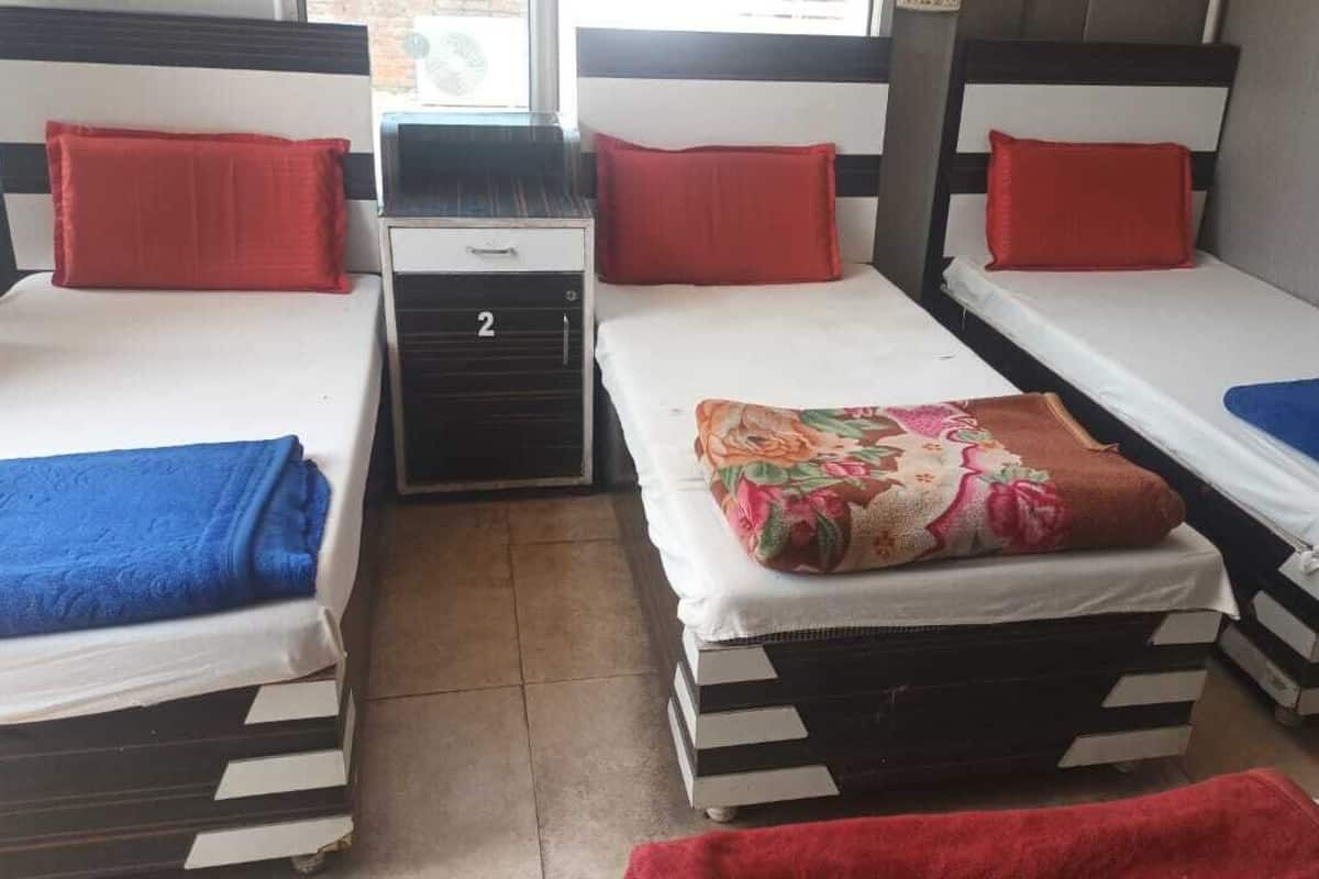 A room with three beds, each with a pillow and a blanket. There is a small table with a drawer in the center.