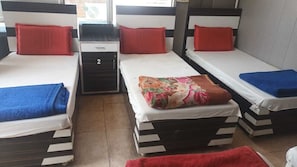 A room with three beds, each with a pillow and a blanket. There is a small table with a drawer in the center.