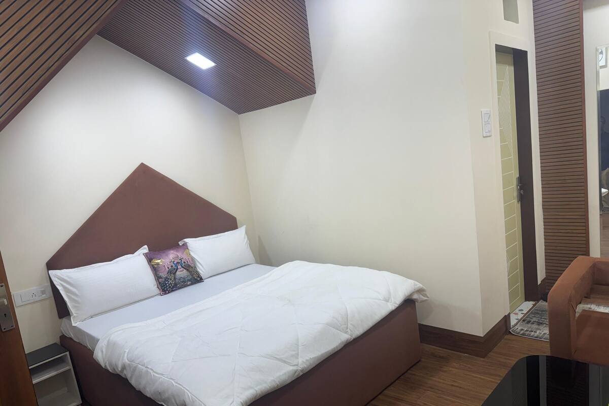 A neatly made bed with a brown headboard, a bedside table, and a small shelf.