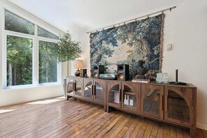 Ein Zimmer mit großem Fenster, einem Holzschrank mit Glastüren, einem Wandteppich und einer Statue.
