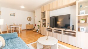 A modern living room with a TV, wooden cabinets, a dining area, and a blue sofa.