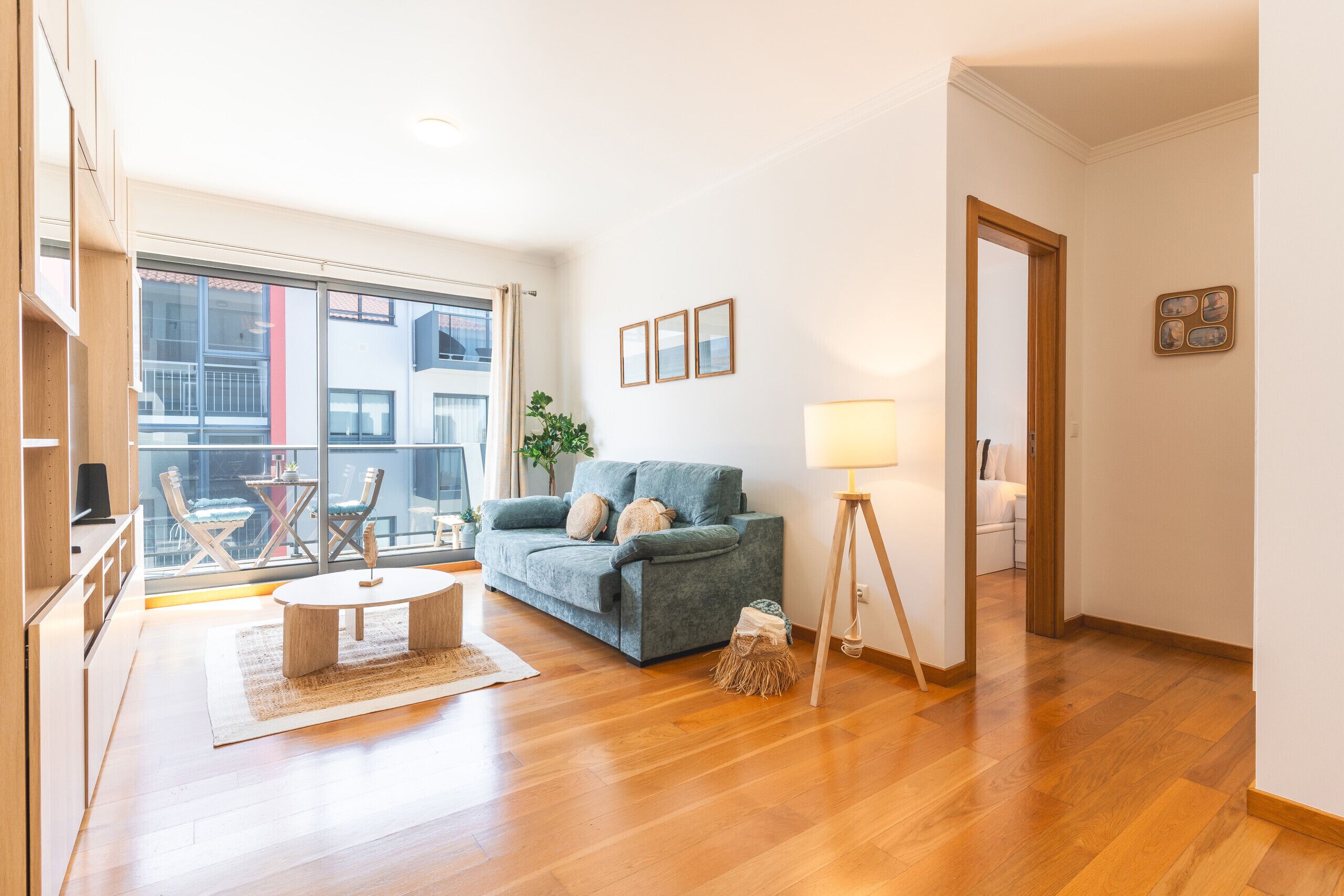 Een moderne woonkamer met een bank, salontafel en lamp. Een groot raam biedt uitzicht op gebouwen.