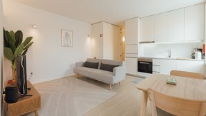 A modern living room with a sofa, a dining table, a kitchen area, and a large plant. - Downtown Elegant Studio by Vacationy (Porto)