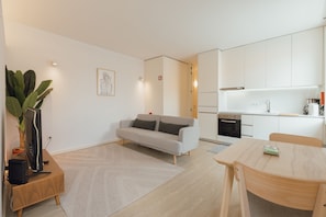 Una sala de estar moderna con un sofá, una mesa de comedor, una zona de cocina y una planta grande.