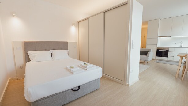 A modern bedroom with a bed, bedside tables, a wardrobe, and a kitchenette. - Downtown Elegant Studio by Vacationy (Porto)
