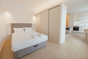 A modern bedroom with a bed, bedside tables, a wardrobe, and a kitchenette. - Downtown Elegant Studio by Vacationy (Porto)