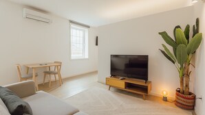 A living room with a sofa, TV, wooden table, chairs, and a potted plant. - Downtown Elegant Studio by Vacationy (Porto)