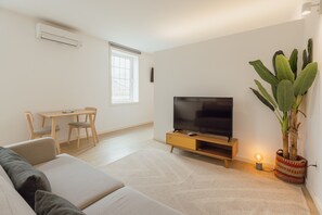 Ein Wohnzimmer mit einer Couch, Fernseher, Holztisch, Stühlen und einem Blumentopf.