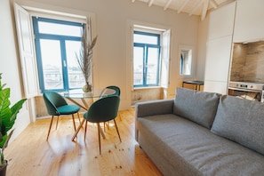 A modern living room with a sofa, two chairs, a glass table, and a view of the city through large windows. - Boavista Charming by Vacationy (Porto)