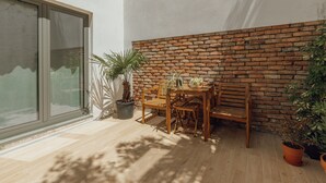Um pátio com mesa e cadeiras de madeira, parede de tijolos e plantas em vasos.