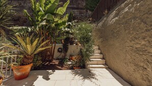 Um espaço ao ar livre pavimentado, com plantas em vasos, um muro de concreto e uma escadaria.