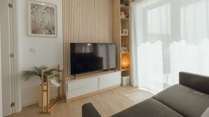 Uma sala de estar moderna com televisão de tela plana, um móvel para TV de madeira, um sofá, um vaso de planta e um painel decorativo na parede.