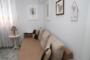 A living room with a beige sofa, a small round table with a lamp, and framed pictures on the wall. - Robert Apartament - City Center Berat (Berat)