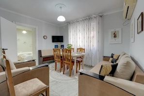 A living room with a dining table, chairs, a sofa, a TV, and a window with curtains.