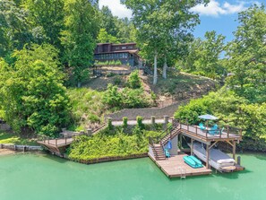 A lakeside property with a wooden dock, a small boat, and a house with a deck. - Lakefront retreat with private dock, lake views, spacious decks, pool table, and sun room! (Pulaski)