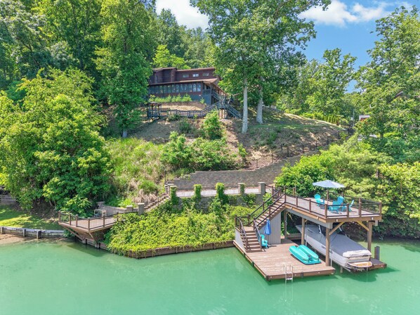 A lakeside property with a wooden dock, a small boat, and a house with a deck.