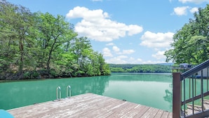 A wooden dock extending into a calm lake surrounded by dense trees, with a clear sky above. - Lakefront retreat with private dock, lake views, spacious decks, pool table, and sun room! (Pulaski)