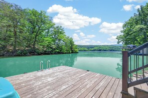 A wooden dock extending into a calm lake surrounded by dense trees, with a clear sky above.