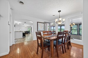 A spacious dining area with a wooden table and chairs, large windows, and a view of the outdoors.