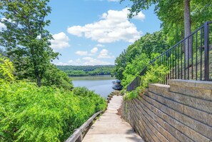A concrete pathway leading to a body of water, surrounded by lush greenery and a stone wall with a metal railing.