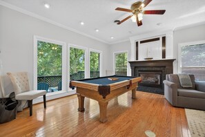 A pool table in a room with large windows, a fireplace, and a ceiling fan.