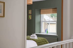 Ein Schlafzimmer mit Fenster, Heizkörper und einem Bett mit grüner Decke.