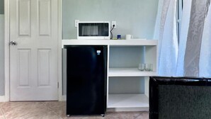 Una kitchenette compacta con microondas, refrigerador y estantes.